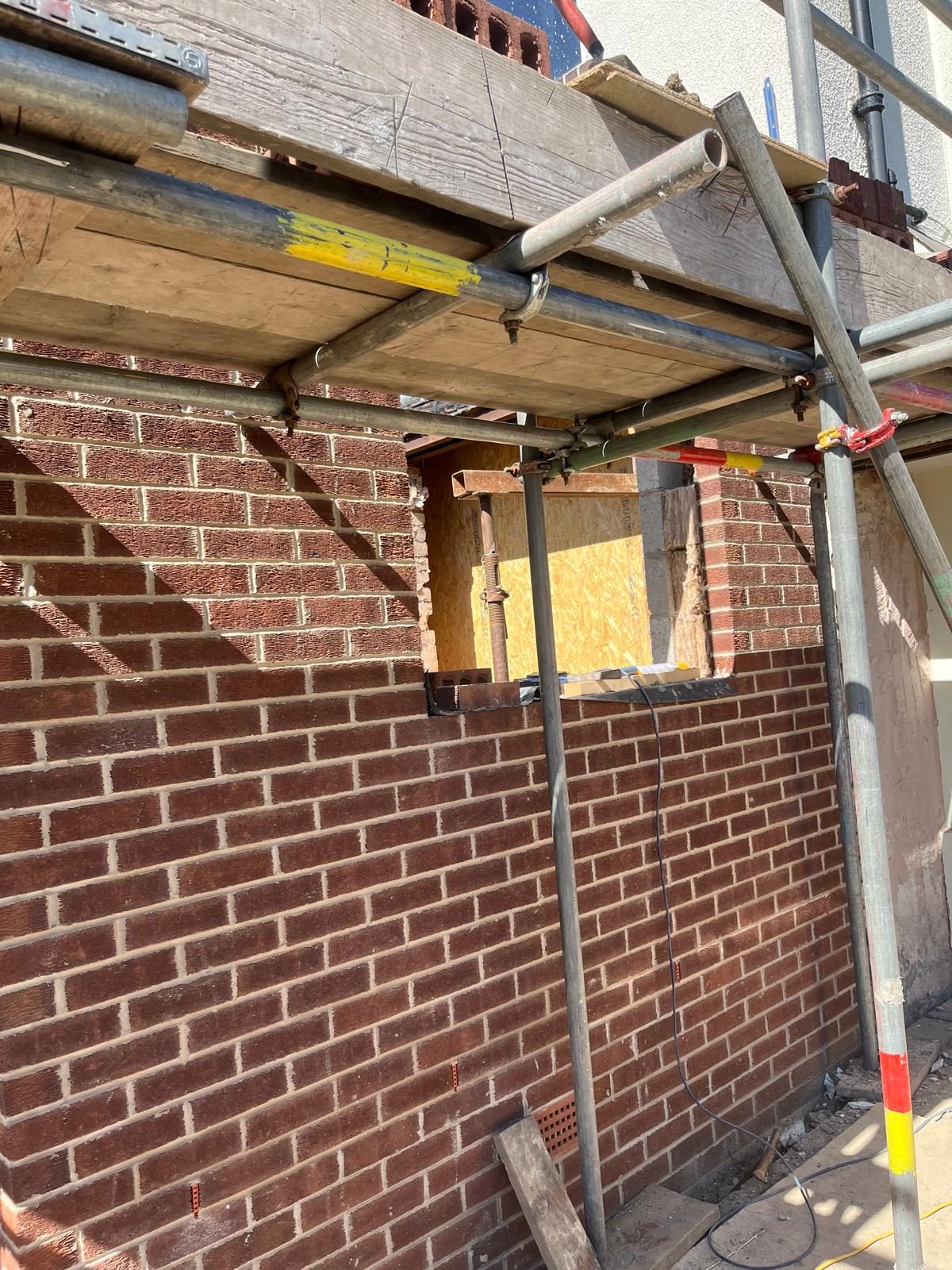 Red brick extension wall being built under scaffold